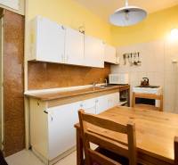 Kuchyně s dřevěným stolem ve 3-pokojovém bytě. Skříňky, sporák, lednička s magnetkami.