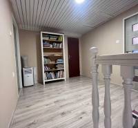 Chodba s podlahou s dřevěným dekorem, knihovnou a světlým dřevěným zábradlím v rodinném domě.