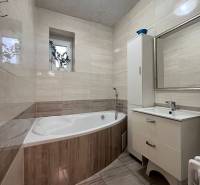 Koupelna s vanou v rodinném domě, obložené stěny, okno s květinou.