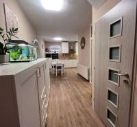 Interiér rodinného domu s kuchyní, bílým nábytkem a podlahou s dřevěným dekorem.