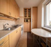 Kuchyně v 2-pokojovém bytě s podlahou s dřevěným dekorem, světlým nábytkem a stolem u okna.