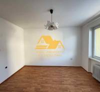 Pokoj v 3-pokojovém bytě s bílými stěnami, podlahou s dřevěným dekorem a radiátorem.