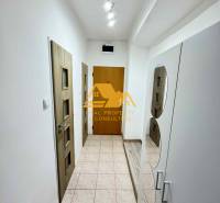 Chodba s bílými stěnami, dlažbou a dřevěnými dveřmi v 3-pokojovém bytě.