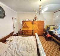 Ložnice v rodinném domě s postelí, skříní a kobercem s geometrickým vzorem.