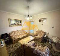 Obývací pokoj v rodinném domě s gaučem a křesly, dekorovaný obrazy.