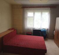 Ložnice v rodinném domě s jednoduchým nábytkem a červenou postelí.