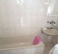 Koupelna s vanou a umyvadlem v rodinném domě, světlé obklady a dlažba.