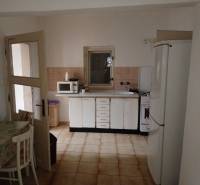 Kuchyně v rodinném domě s bílými skříňkami, mikrovlnkou a ledničkou.