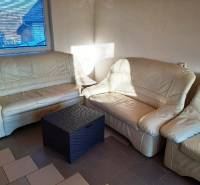 Béžová sedačka v chatě s ratanovým stolkem, sluneční světlo přes okno.