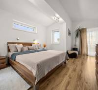 Ložnice v rodinném domě s postelí, dekorativními prvky a podlahou s dřevěným dekorem.