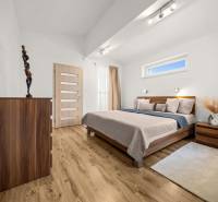 Ložnice s podlahou s dřevěným dekorem, postelí a komodou v rodinném domě.