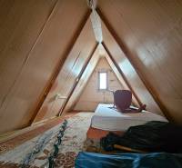 Podkroví chaty s matrací a židlí, dřevěný dekor, světlé stěny.