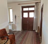 Chodba rodinného domu s dlaždicovou podlahou, křeslem a závěsem.