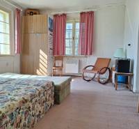 Pokoj s květinovou pohovkou, křeslem, skříní a růžovými závěsy v rodinném domě.