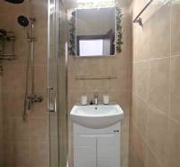 Koupelna v rekreačním apartmánu se sprchovým koutem a umyvadlem, obložená světlými dlaždicemi.