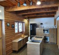 Rustikální kuchyně v chatě s dřevěnými dekoracemi, světlým nábytkem a stropními trámy.