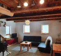 Interiér chaty s kachlovými kamny, pohovkou a dřevěným stropem z masivních trámů.