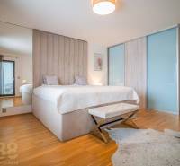 Ložnice v rodinném domě s postelí, podlahou s dřevěným dekorem a kožešinovým kobercem.