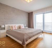 Ložnice v rodinném domě s postelí, nočními stolky a podlahou s dřevěným dekorem.