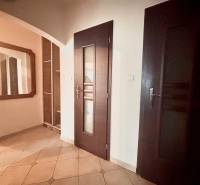 Chodba v 3-pokojovém bytě s dlažbou, zrcadlem a tmavými dveřmi.