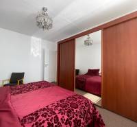 Ložnice s velkou skříní, lustrem a postelí v 3-pokojovém bytě.