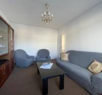 Obývací pokoj v 3pokojovém bytě s pohodlnou pohovkou, křesly a vitrínou.