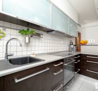 Kuchyně v 3-pokojovém bytě s bílými obkladačkami a tmavými skříňkami.