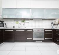 Kuchyně ve 3-pokojovém bytě se spotřebiči a tmavým kuchyňským nábytkem s bílými kachličkami.