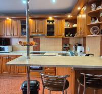 Kuchyně v rodinném domě s dřevěnými skříňkami, barovým pultem a spotřebiči.