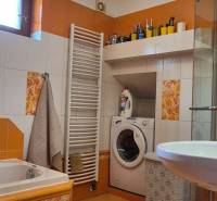 Koupelna v rodinném domě s pračkou, sprchovým koutem, vanou a barevnými obklady.