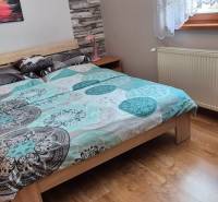 Ložnice v rodinném domě s postelí, radiátorem a podlahou s dřevěným dekorem.