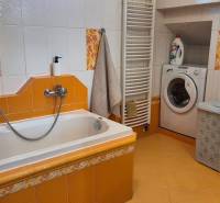 Koupelna v rodinném domě s vanou, umyvadlem, pračkou a žlutou dlažbou.