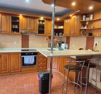 Kuchyně v rodinném domě s dřevěným dekorem, vybavená spotřebiči a barovým pultem.