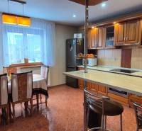 Kuchyně s jídelním stolem v rodinném domě, dřevěné skříňky a podlaha s dlažbou.