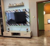 Obývací pokoj v rodinném domě s dřevěným dekorem podlahy a velkou televizí na stěně.