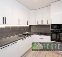 Kuchyně v 3-pokojovém bytě s bílými skříňkami a spotřebiči, podlaha s dřevěným dekorem.