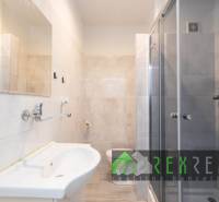 Koupelna v 3-pokojovém bytě se sprchovým koutem, umyvadlem a světlými dlaždicemi.