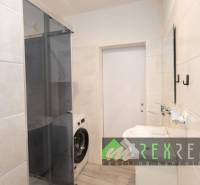 Koupelna ve 3-pokojovém bytě se sprchovým koutem a pračkou, obklady na stěnách.