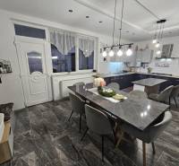 Jídelní prostor s kamenným stolem, šedými židlemi a závěsnými světly v rodinném domě.