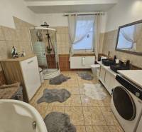 Koupelna v rodinném domě s vanou, sprchovým koutem a pračkou.