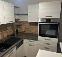 Kuchyň v 2-pokojovém bytě, s podlahou s dřevěným dekorem a vestavnou troubou.