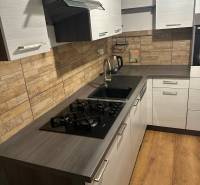 Kuchyně v 2-pokojovém bytě s plynovým sporákem, moderním obkladem a podlahou s dřevěným dekorem.