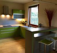 Kuchyně v rodinném domě se zelenými skříňkami a barovým pultem, podlaha s dřevěným dekorem.