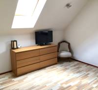 Interiér rodinného domu s komodou, křeslem a podlahou s dřevěným dekorem.