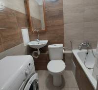 Koupelna v 1-pokojovém bytě s vanou, umyvadlem a pračkou, obložená keramickými dlaždicemi.