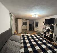 Ložnice v rodinném domě s manželskou postelí, bílým nábytkem a vzorovanou přikrývkou.