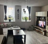 Obývací pokoj v rodinném domě s pohovkou, televizí a podlahou s dřevěným dekorem.