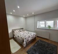 Ložnice v rodinném domě s postelí, oknem a podlahou s dřevěným dekorem.