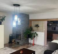 Interiér rodinného domu s krbem, závěsnými svítidly a podlahou s dřevěným dekorem.