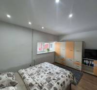 Ložnice v rodinném domě s postelí, skříní a televizí. Podlaha s dřevěným dekorem.